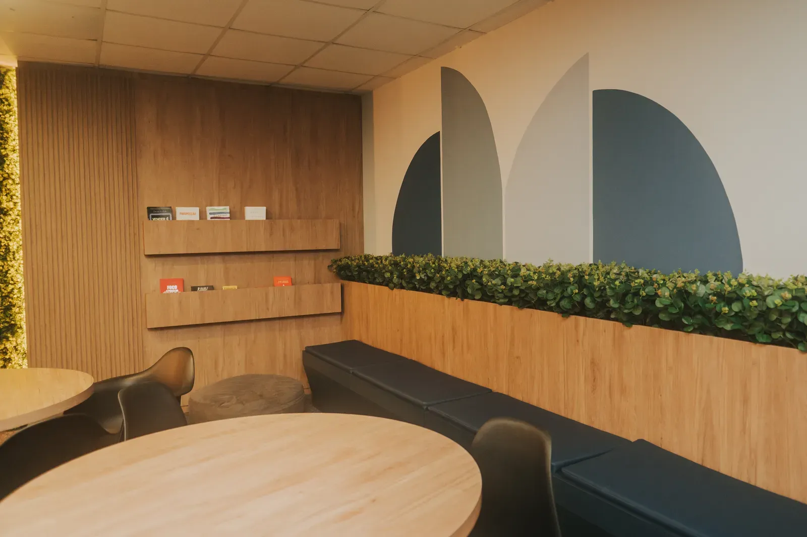 Área de convivência da escola, com mesas redondas, banco estofado e jardim vertical